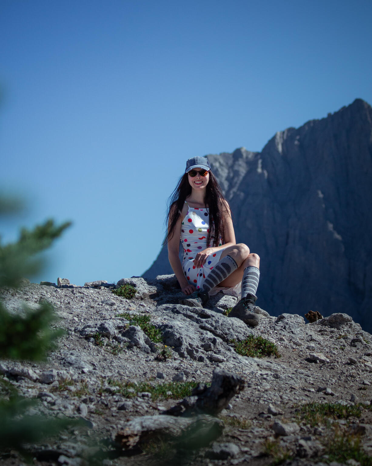 Layla Messner in a polkadot dress in the alpine by David Dethlefs Layla Messner, the autistic art activist who grew up in the wilderness. A smiling brunette in a polkadot dress and a denim ball cap and hiking boots, sitting in the alpine. Canmore, Alberta, Canada. Photography by David Dethlefs