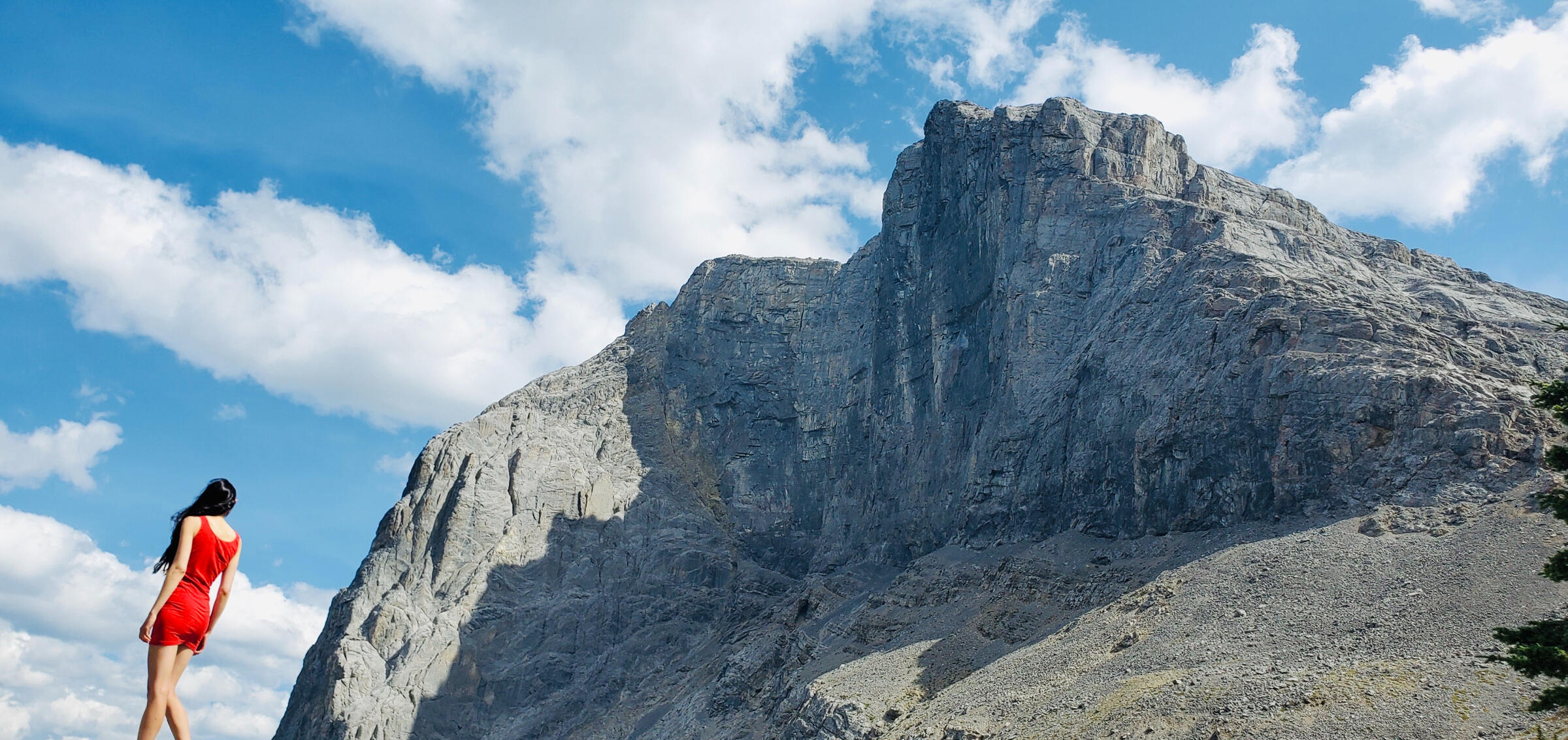 A brunette in a red dress next to a mountain face. Photography by Kelly's Perspective.