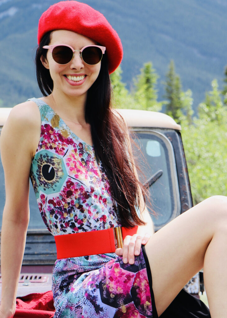 Layla Messner sitting on a vintage yj Jeep, wearing a dress printed with her colorful art and a raspberry beret. Photo by Kelly's Perspective