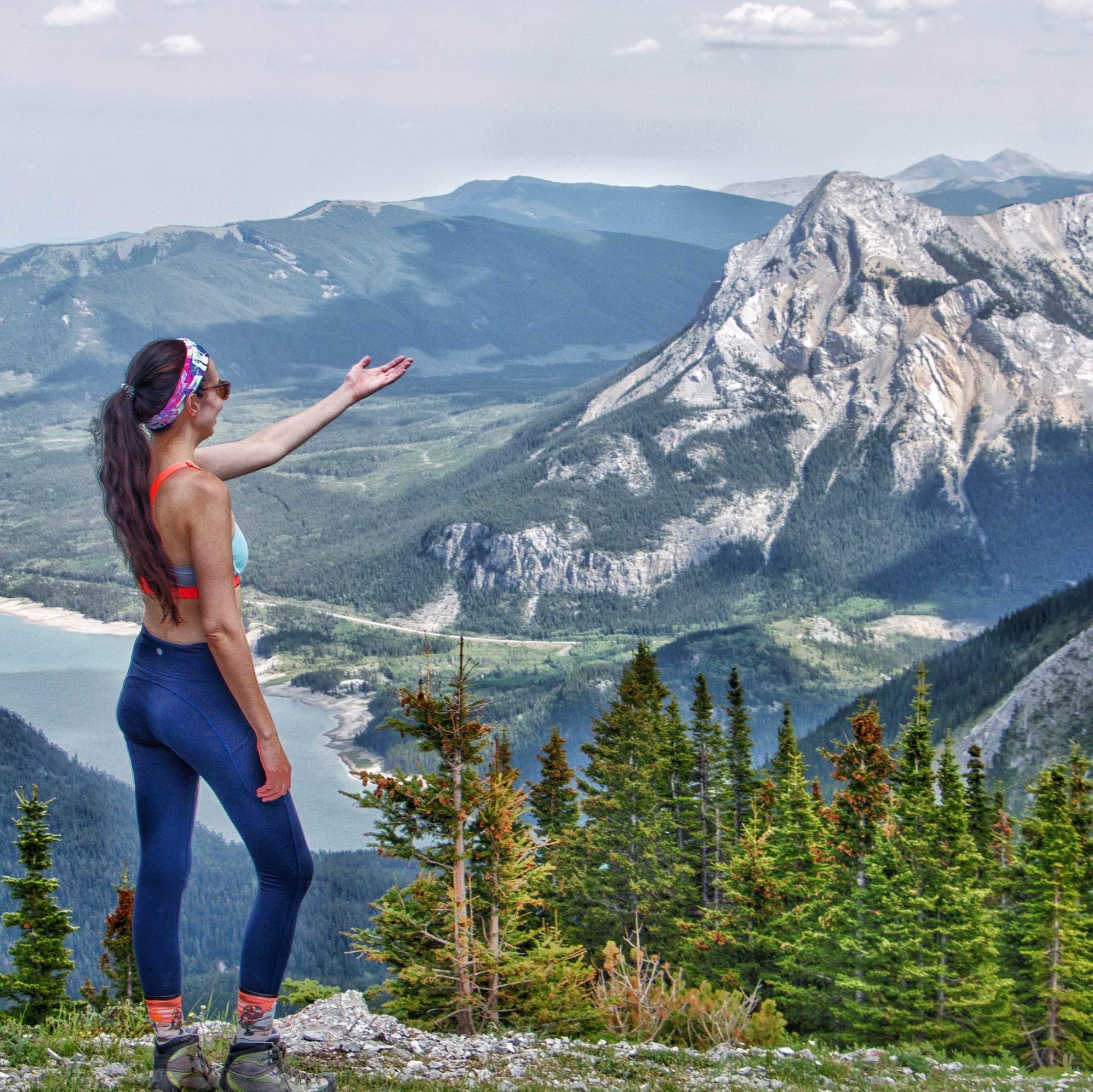 Layla Messner with one hand outstretched on a mountain summit by Kelly's Perspective