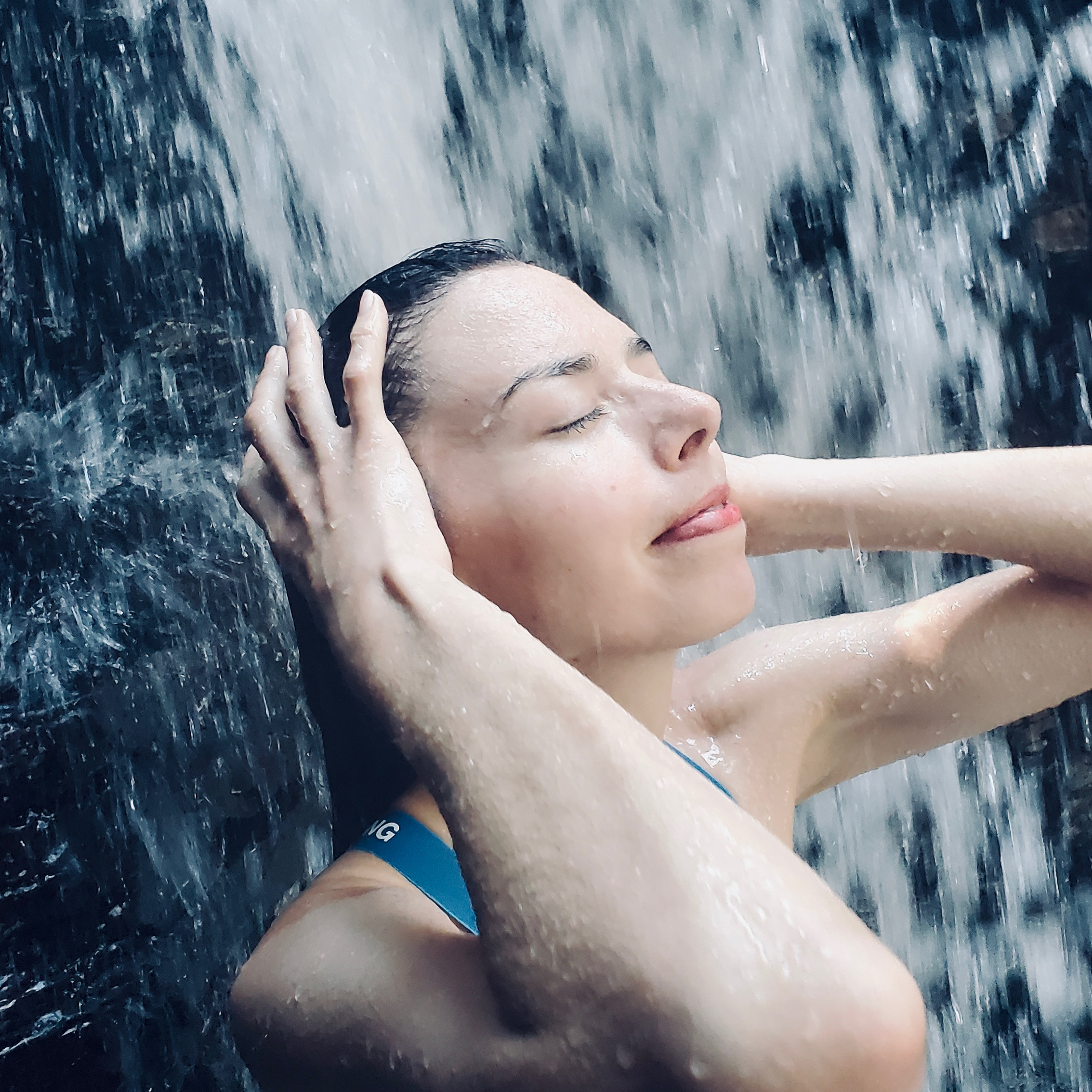 Layla Messner bathing in a waterfall in a blue sports bra by Kelly's Perspective