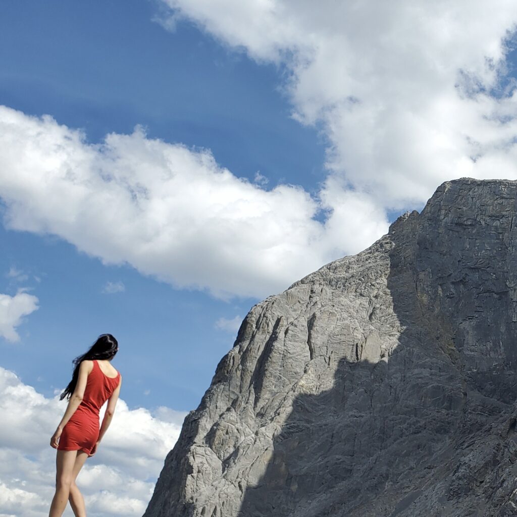 Layla Messner, The Instinctual Woman, wearing a red sheath dress next to a mountain face. Photograph by Kelly's Perspective.