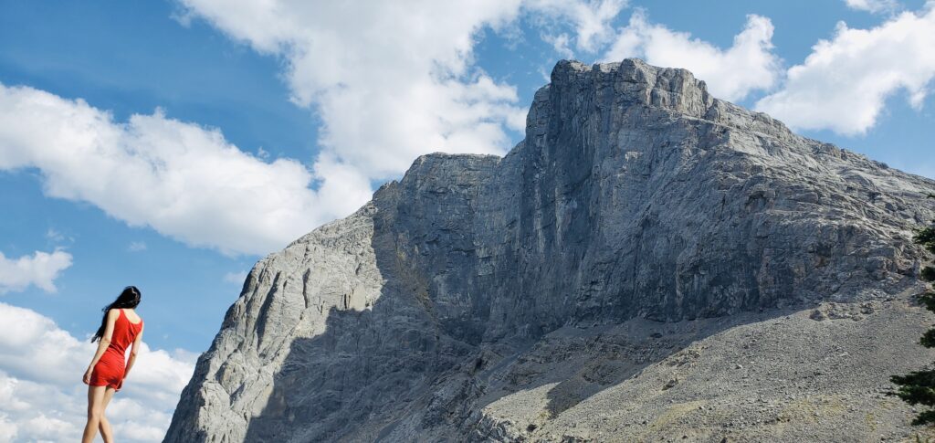 Layla Messner, a slender model in a red dress next to a huge mountain face. Photo by Kelly's Perspective